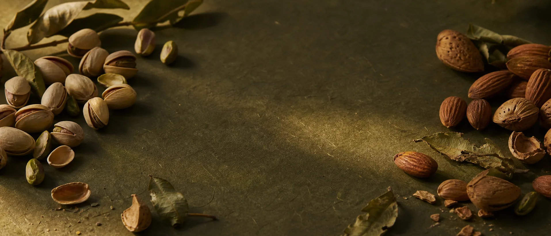 Pistachios and almonds arranged along the edges of a dark olive work surface
